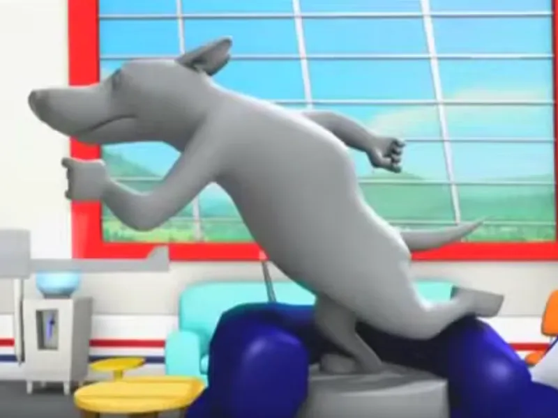 A grey statue of a running dog standing on a pedestal beside a blue armchair